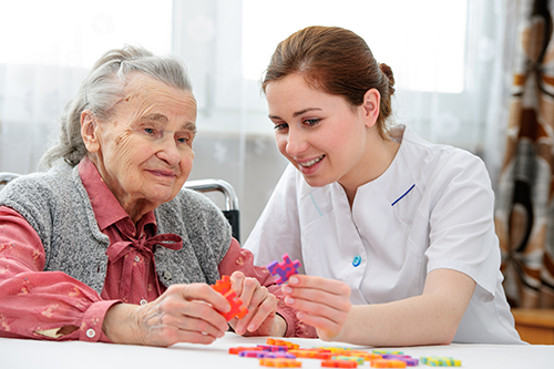 Elderly woman putting color puzzle together with young nurse in white scrubs