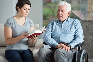 Daughter sitting next to father in wheelchair reading a book with him